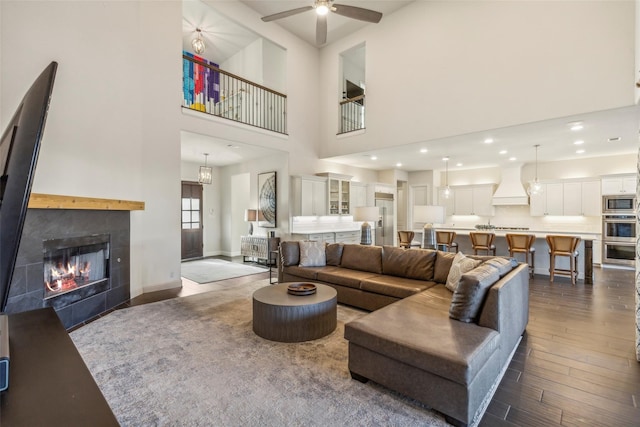 living room featuring ceiling fan, dark hardwood / wood-style floors, a tile fireplace, and a towering ceiling