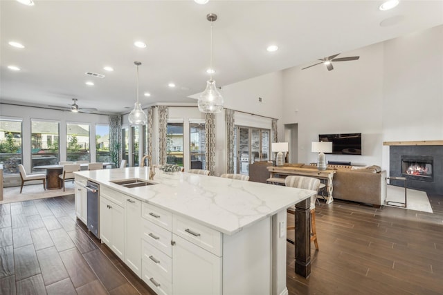 kitchen featuring white cabinetry, light stone countertops, pendant lighting, and a center island with sink