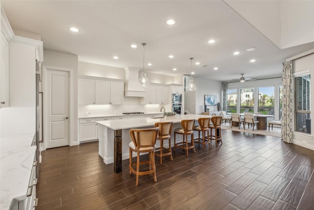 kitchen with ceiling fan, a spacious island, custom exhaust hood, hanging light fixtures, and white cabinets