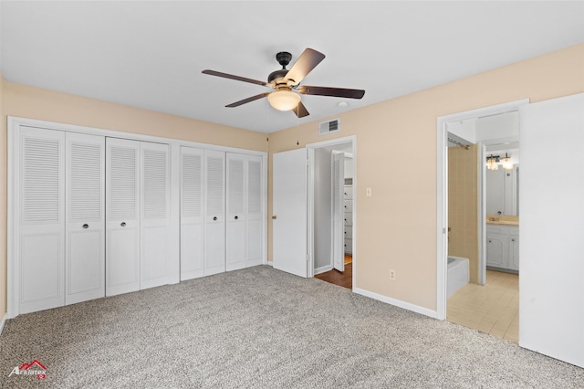 unfurnished bedroom with ceiling fan, ensuite bathroom, light carpet, and multiple closets