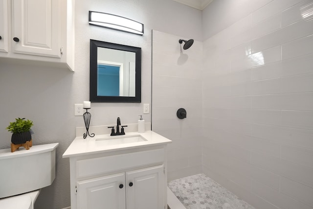full bath with toilet, a textured wall, tiled shower, and vanity