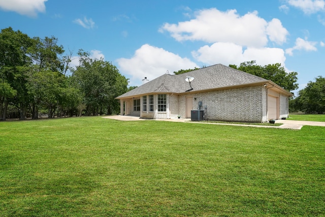 back of house featuring brick siding, a lawn, central AC unit, a garage, and driveway