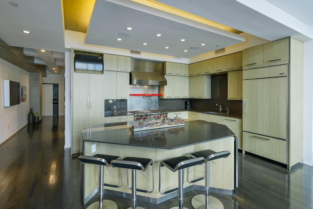 kitchen with a spacious island, paneled built in refrigerator, dark wood-type flooring, wall chimney range hood, and sink