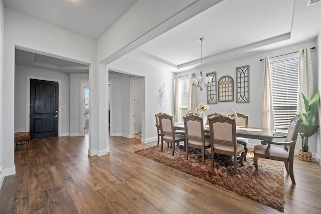 dining room with dark hardwood / wood-style flooring, a tray ceiling, and a chandelier