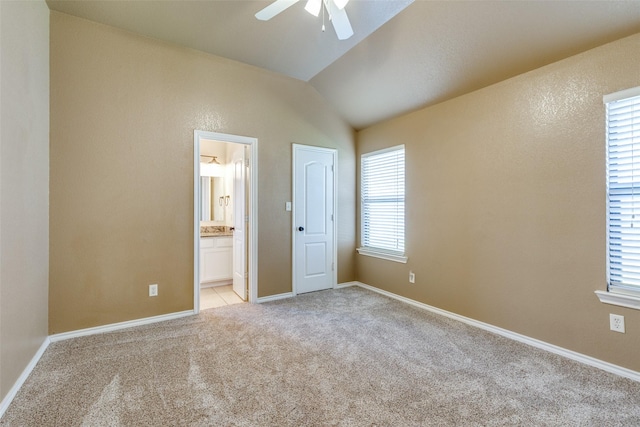 unfurnished bedroom featuring ceiling fan, light colored carpet, connected bathroom, and vaulted ceiling