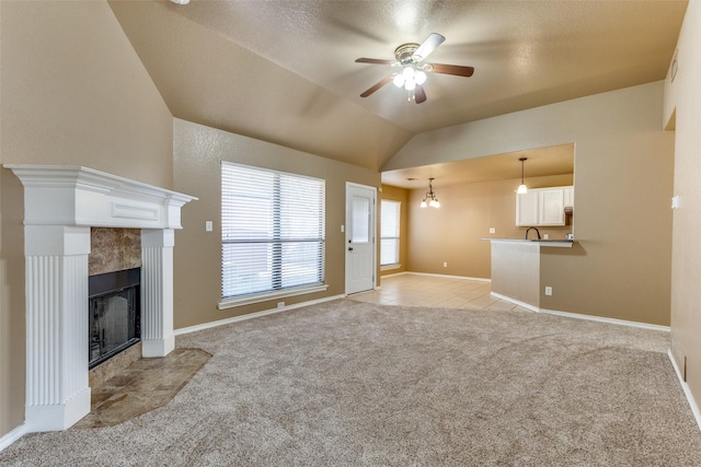 unfurnished living room with vaulted ceiling, light colored carpet, ceiling fan with notable chandelier, and a tile fireplace