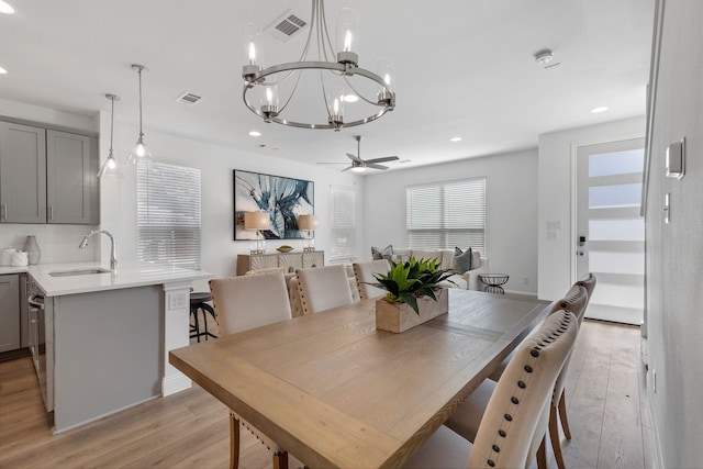 dining area featuring ceiling fan with notable chandelier, sink, and light wood-type flooring