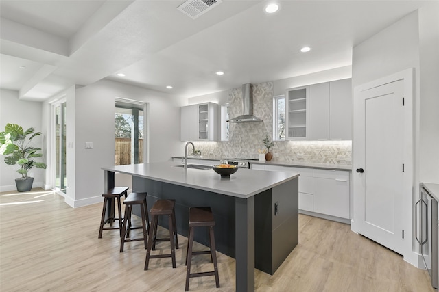 kitchen with wall chimney exhaust hood, white cabinetry, sink, a breakfast bar, and a center island with sink