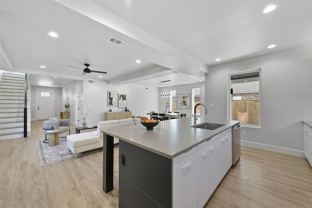 kitchen featuring white cabinetry, an island with sink, light wood-type flooring, stainless steel dishwasher, and sink