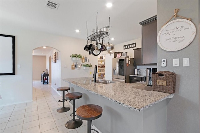 kitchen with stainless steel fridge with ice dispenser, light tile patterned floors, kitchen peninsula, dark brown cabinets, and sink