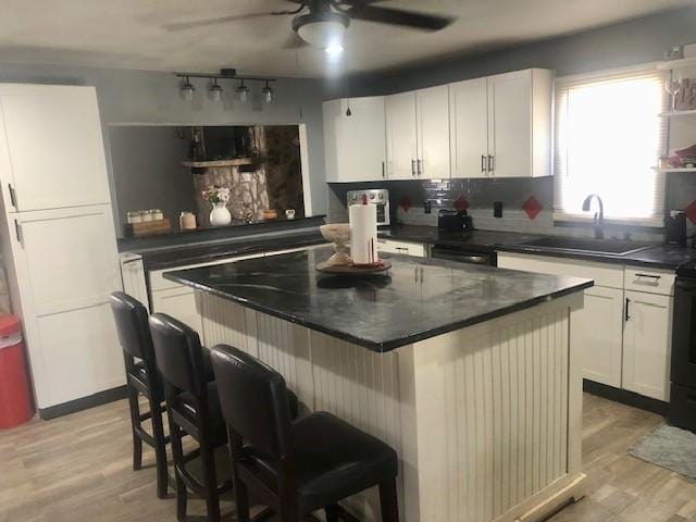 kitchen featuring a kitchen island, white cabinetry, light hardwood / wood-style floors, sink, and a breakfast bar