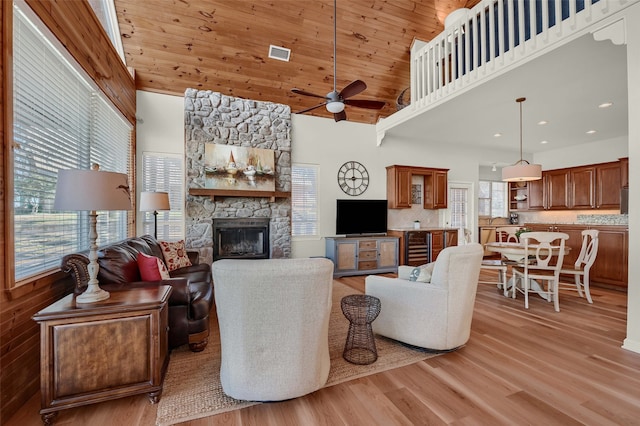 living room featuring a stone fireplace, high vaulted ceiling, wine cooler, wooden ceiling, and light hardwood / wood-style flooring