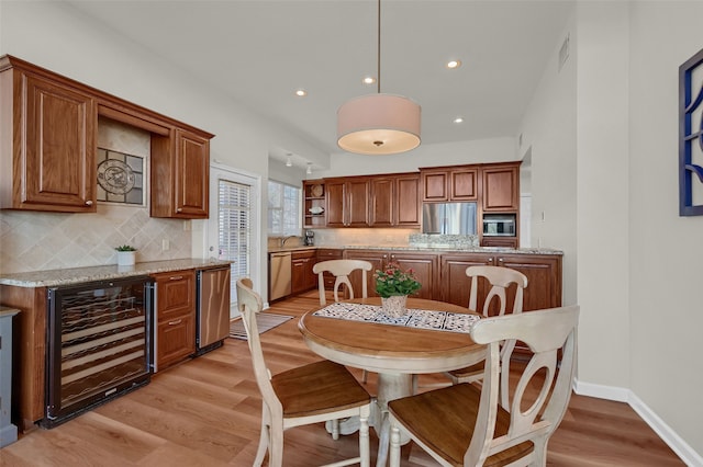 kitchen featuring pendant lighting, stainless steel appliances, beverage cooler, and light stone counters