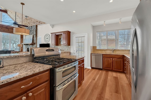 kitchen with pendant lighting, stainless steel appliances, light stone counters, light hardwood / wood-style floors, and decorative backsplash