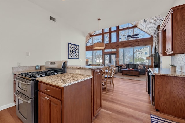 kitchen with range with two ovens, pendant lighting, light stone counters, and light wood-type flooring