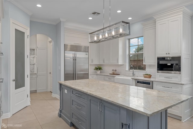 kitchen featuring decorative light fixtures, a center island, built in refrigerator, white cabinets, and light stone counters