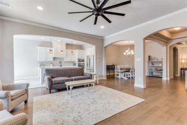 living room with ceiling fan with notable chandelier, sink, hardwood / wood-style flooring, and ornamental molding