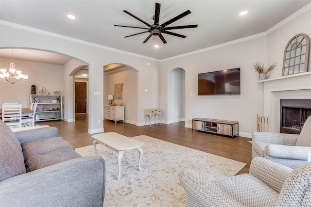 living room featuring crown molding, a fireplace, dark hardwood / wood-style flooring, and ceiling fan with notable chandelier