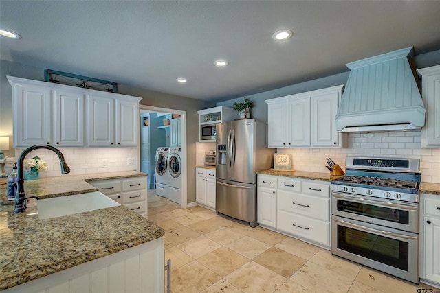 kitchen with white cabinets, appliances with stainless steel finishes, washing machine and dryer, custom exhaust hood, and sink