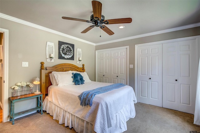 carpeted bedroom featuring ceiling fan, multiple closets, and crown molding