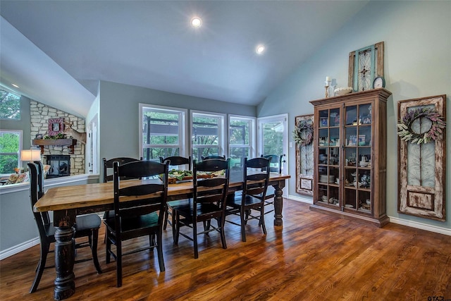 dining space featuring vaulted ceiling, dark hardwood / wood-style floors, and a stone fireplace