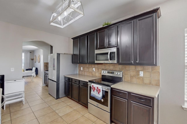 kitchen with pendant lighting, light tile patterned floors, appliances with stainless steel finishes, backsplash, and dark brown cabinetry