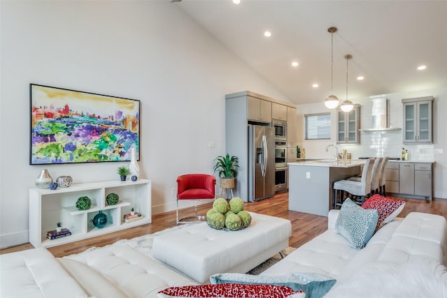 living room with light hardwood / wood-style floors, sink, and high vaulted ceiling