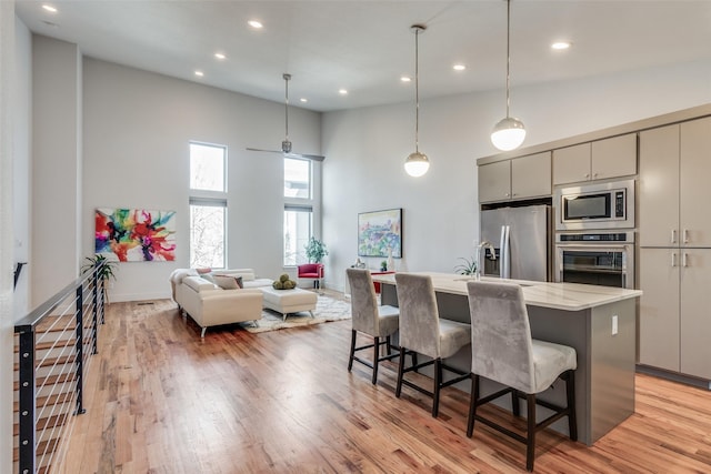 kitchen with a center island with sink, appliances with stainless steel finishes, a high ceiling, a kitchen breakfast bar, and light wood-type flooring