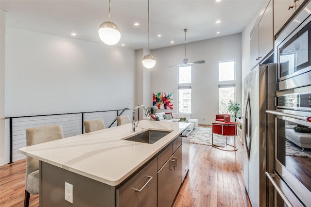 kitchen featuring stainless steel appliances, light hardwood / wood-style floors, sink, hanging light fixtures, and a center island with sink