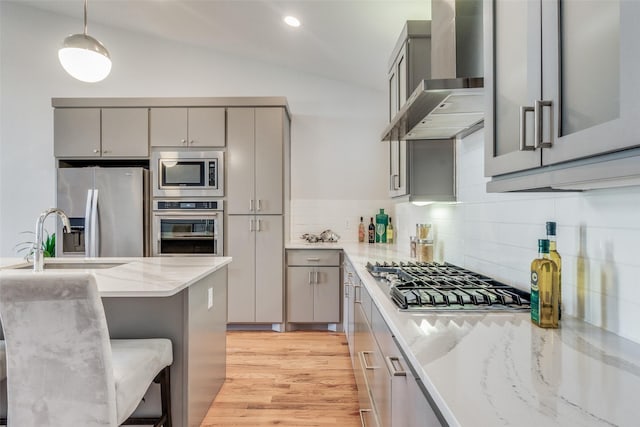 kitchen with appliances with stainless steel finishes, decorative light fixtures, wall chimney range hood, vaulted ceiling, and gray cabinetry