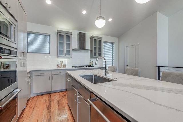 kitchen with wall chimney exhaust hood, sink, hanging light fixtures, backsplash, and vaulted ceiling