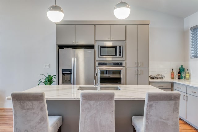 kitchen with a breakfast bar area, stainless steel appliances, gray cabinetry, hanging light fixtures, and a kitchen island