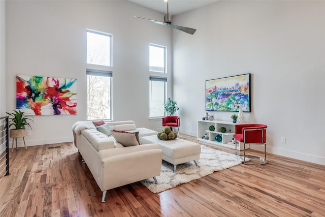 living room featuring ceiling fan, a towering ceiling, and light wood-type flooring