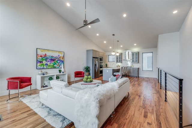 living room with high vaulted ceiling, sink, light hardwood / wood-style flooring, and ceiling fan