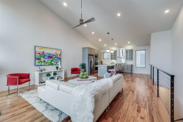 living room featuring ceiling fan, light hardwood / wood-style flooring, sink, and high vaulted ceiling