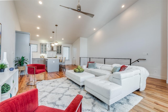 living room with ceiling fan, light hardwood / wood-style floors, high vaulted ceiling, and sink