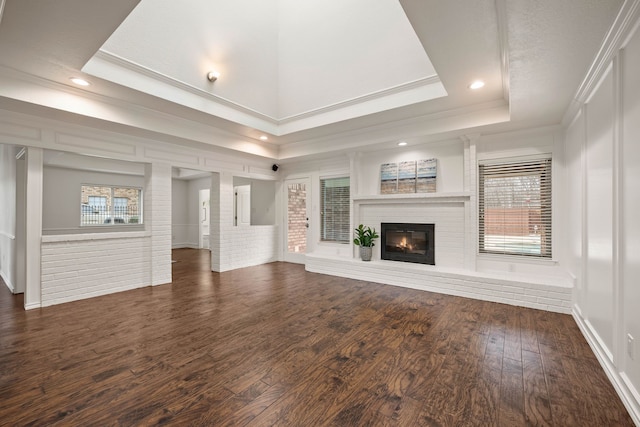 unfurnished living room with a brick fireplace, a raised ceiling, dark wood-type flooring, ornamental molding, and brick wall