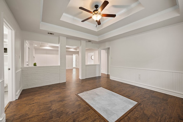 unfurnished room with ceiling fan, a tray ceiling, dark hardwood / wood-style floors, and ornamental molding