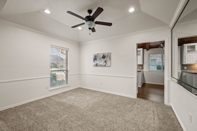 spare room featuring vaulted ceiling, a raised ceiling, ornamental molding, carpet flooring, and ceiling fan