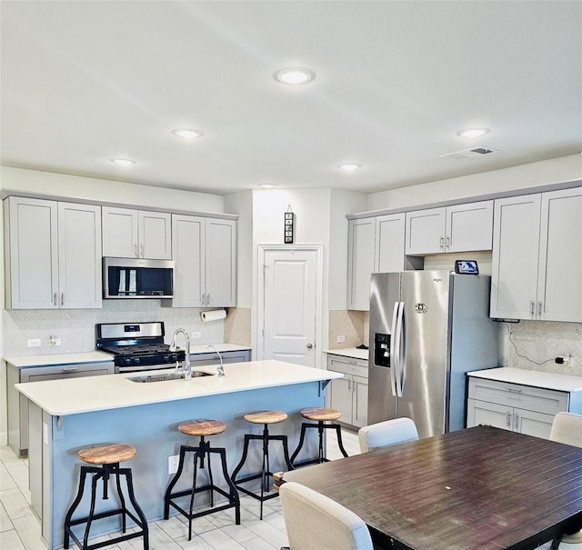 kitchen with a kitchen island with sink, sink, stainless steel appliances, and a kitchen bar