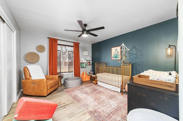 bedroom featuring ceiling fan, light wood-type flooring, a closet, and a crib