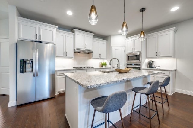 kitchen with white cabinets, stainless steel appliances, sink, a kitchen island with sink, and light stone counters