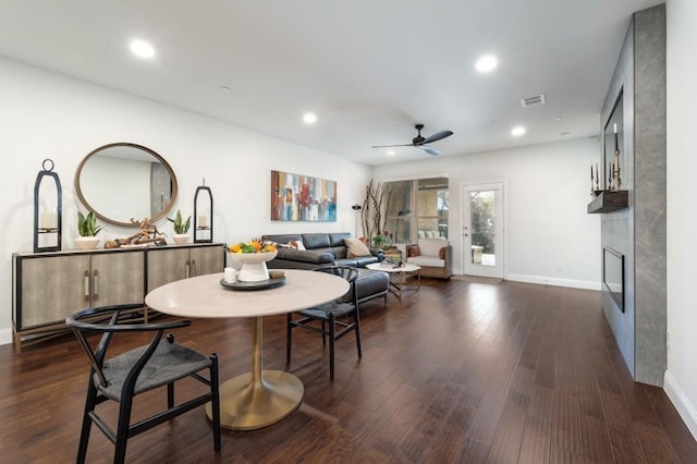 dining space featuring ceiling fan, dark wood-type flooring, and a fireplace