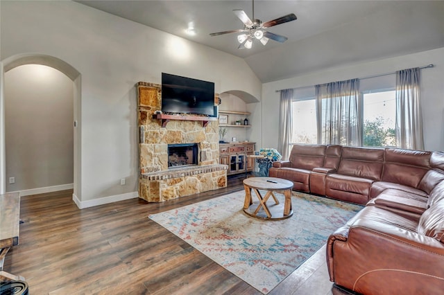 living room featuring ceiling fan, dark hardwood / wood-style floors, a stone fireplace, and lofted ceiling