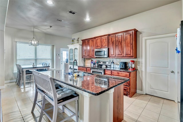 kitchen with decorative light fixtures, stainless steel appliances, an island with sink, sink, and light tile patterned floors