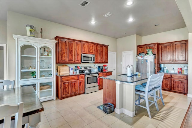 kitchen featuring light tile patterned flooring, sink, stainless steel appliances, and a center island with sink