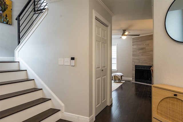 stairway featuring ceiling fan, ornamental molding, a fireplace, and wood-type flooring