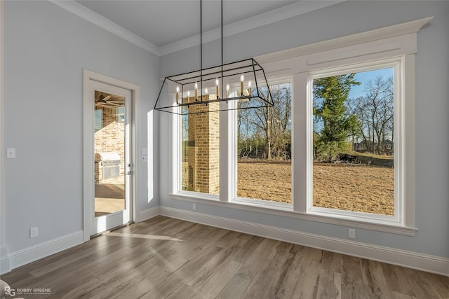 unfurnished dining area featuring ornamental molding, an inviting chandelier, baseboards, and wood finished floors