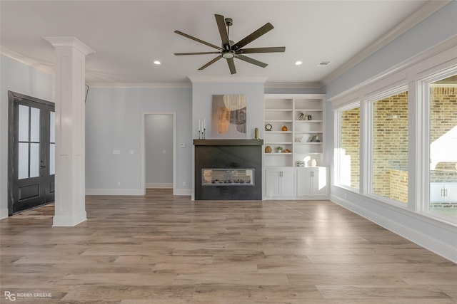 unfurnished living room featuring decorative columns, ornamental molding, light wood-style flooring, and a glass covered fireplace