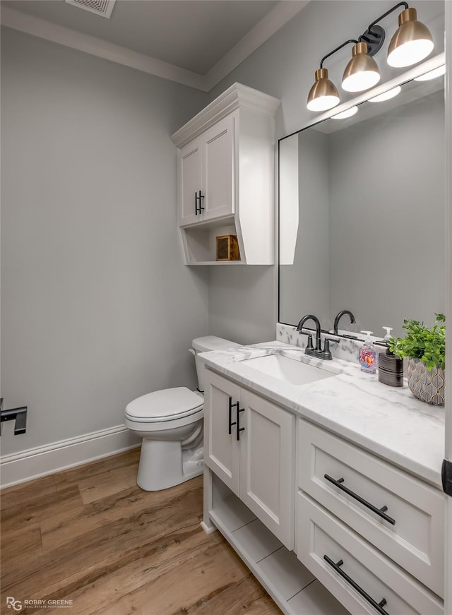 half bathroom with baseboards, visible vents, toilet, wood finished floors, and vanity